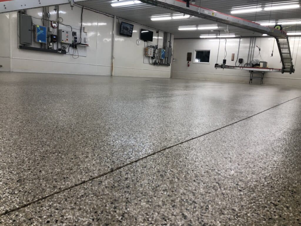 The image shows an empty industrial room with a shiny epoxy floor, white walls, electrical panels, a ladder, and a table against the far wall.