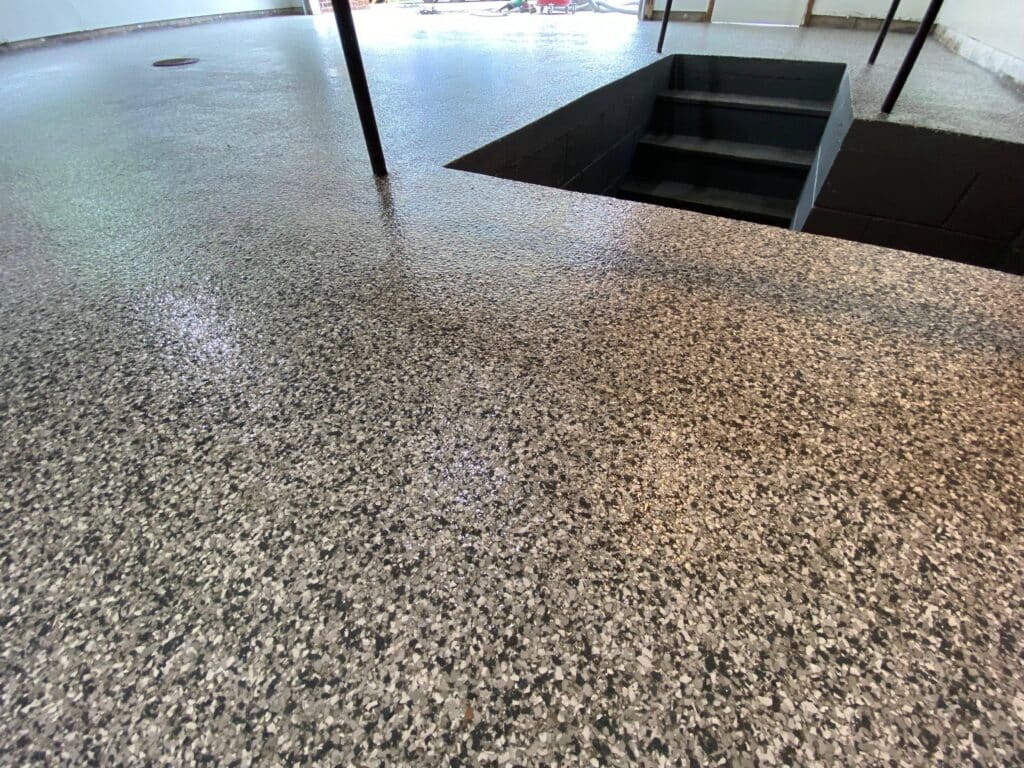 This image shows a speckled terrazzo floor leading to a dark rectangular pit with stairs descending, likely an architectural feature or installation.
